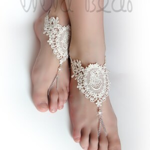 May include: White lace barefoot sandals with silver chains and a crystal embellishment.