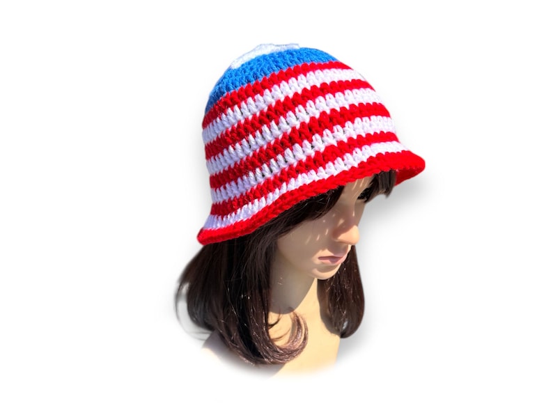 May include: A red, white, and blue crochet bucket hat. The hat features alternating red and white stripes with a blue crown and a red brim. The hat is handmade and has a classic, casual style.