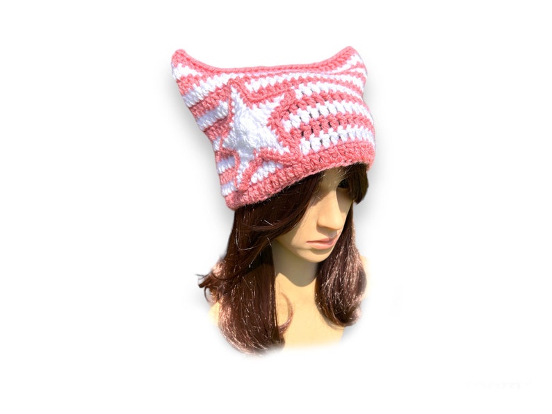 May include: A pink and white crocheted hat with pointed ears and a white star design on the front. The hat is made of yarn and is designed to be worn on the head. The hat is a unique and stylish accessory.