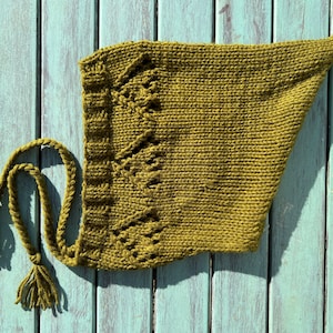 May include: A green knitted hooded scarf with a long tassel. The scarf is made of a soft, textured yarn and has a simple, elegant design.