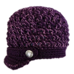 May include: A purple crocheted hat with a pink yarn detail and a silver button. The hat has a brim that is folded down on one side.