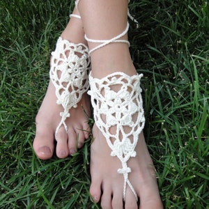 May include: White crocheted barefoot sandals with delicate floral designs and ties that wrap around the ankles.