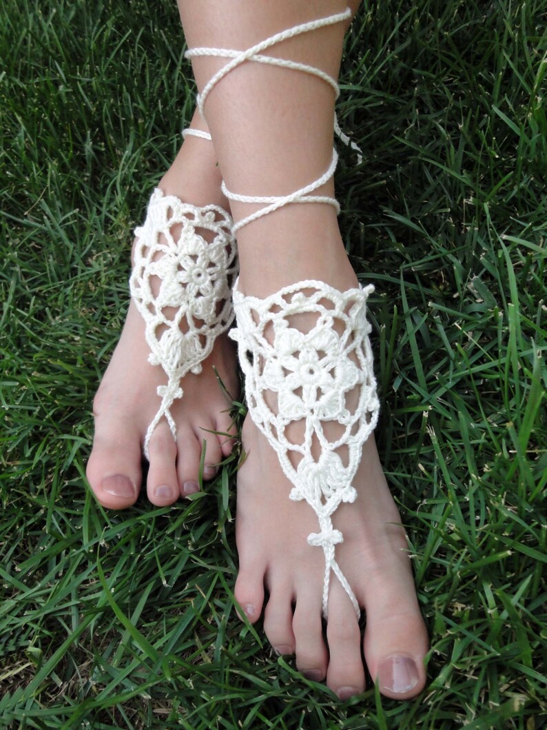 May include: White crocheted barefoot sandals with delicate floral designs and ties that wrap around the ankles.