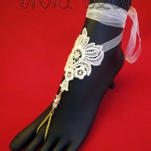 May include: White lace foot jewelry with a gold chain and clear rhinestones. The jewelry is tied with a white ribbon.