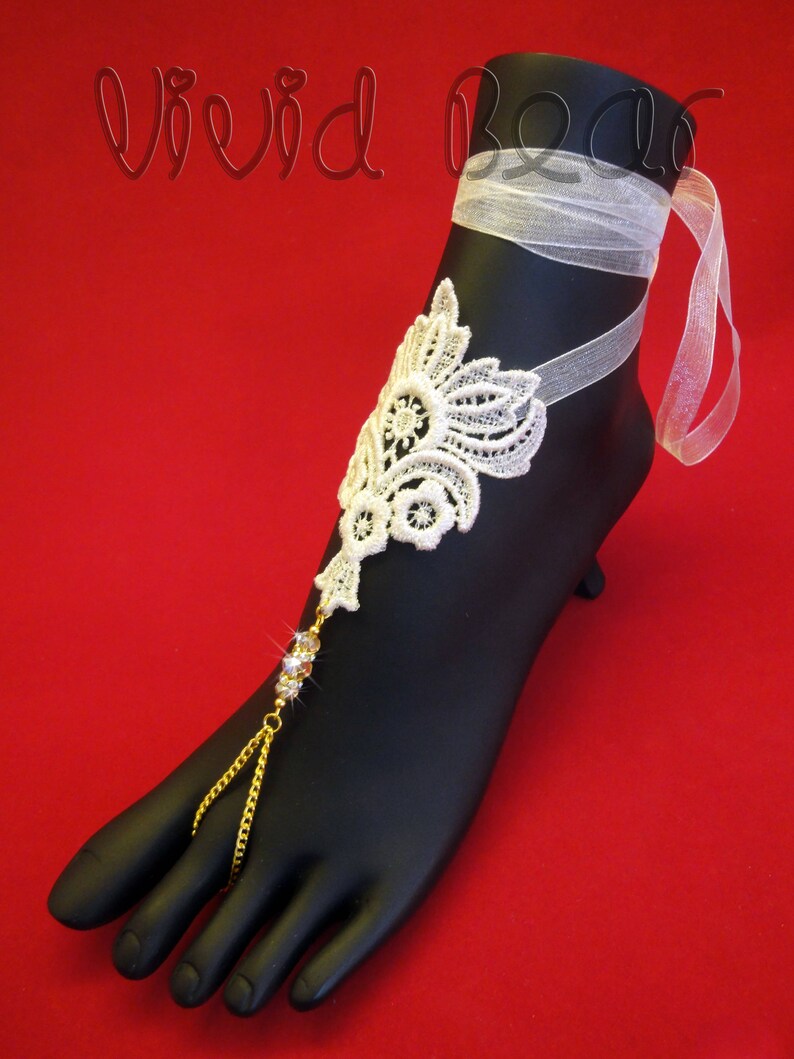 May include: White lace foot jewelry with a gold chain and clear rhinestones. The jewelry is tied with a white ribbon.