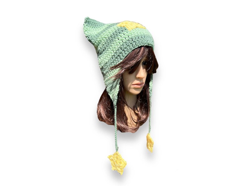 May include: A green and yellow crocheted hat with ear flaps and star-shaped tassels. The hat is made with a textured stitch and has a star design on the top.