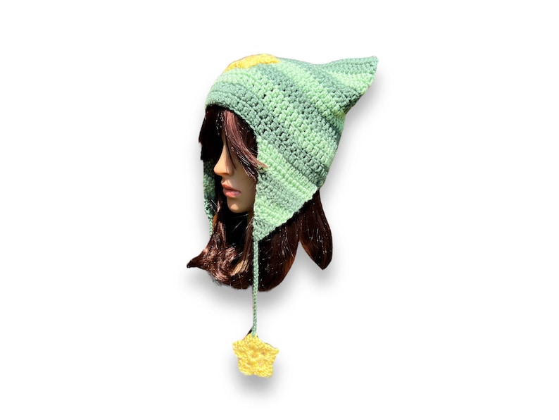 May include: A green and yellow crocheted hat with a pointed ear and a star-shaped tassel. The hat is made with a striped pattern and has a soft, cozy texture.