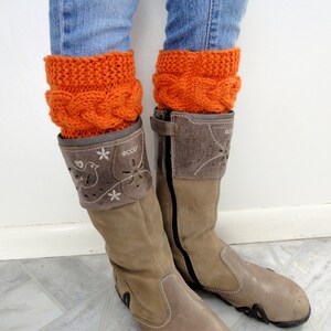 May include: A pair of brown leather boots with a zipper on the side. The boots are worn with orange knitted leg warmers and blue jeans.