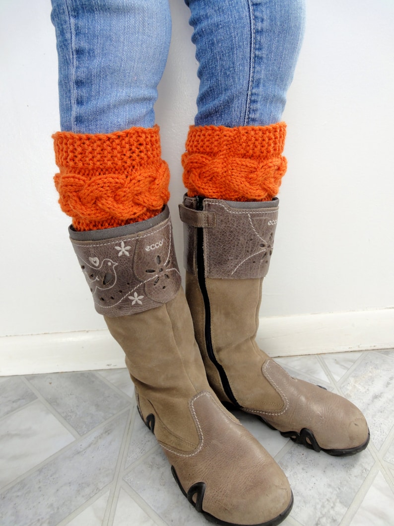 May include: A pair of brown leather boots with a zipper on the side. The boots are worn with orange knitted leg warmers and blue jeans.