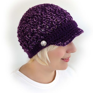 May include: Purple crocheted beanie with a brim and a silver button. The beanie is made with a textured stitch.