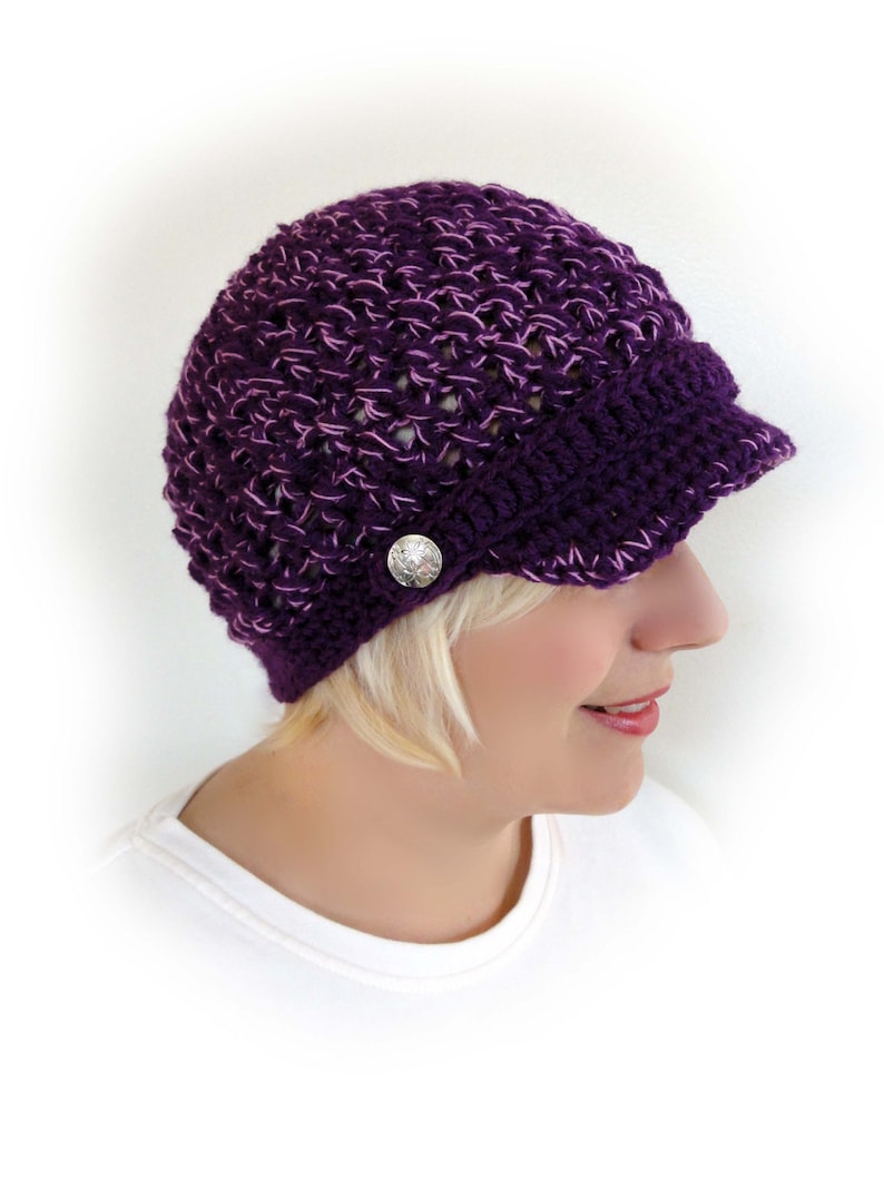 May include: Purple crocheted beanie with a brim and a silver button. The beanie is made with a textured stitch.