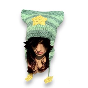 May include: A green and yellow striped crocheted hat with a star on the front and two star-shaped ear flaps.