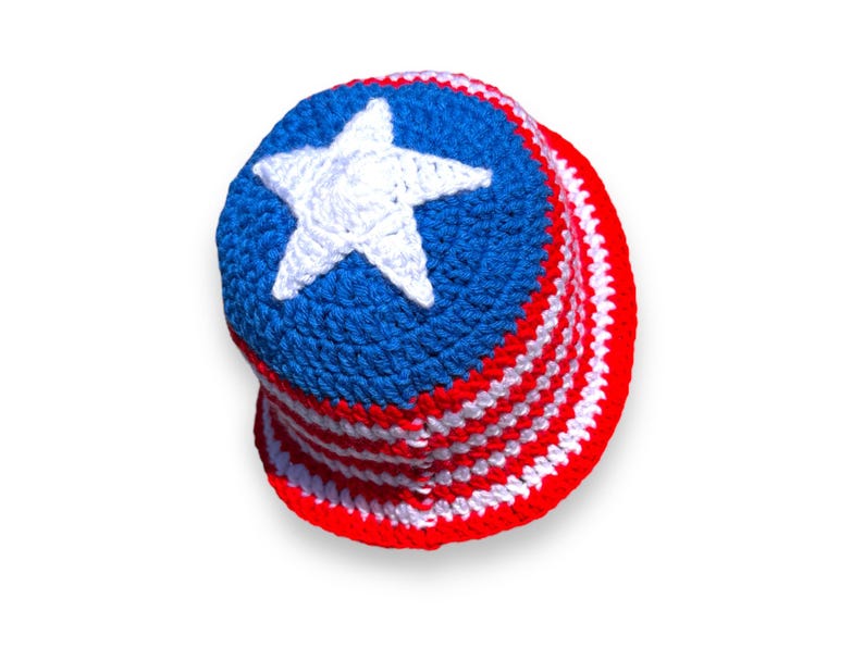 May include: A handmade crochet bucket hat in red, white, and blue, featuring a white star on a blue crown. The hat's brim has alternating red and white stripes, evoking a patriotic theme.