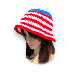 May include: A red, white, and blue crochet bucket hat. The hat features horizontal stripes of red and white, with a blue band at the top. The brim is red. This handmade hat is a stylish accessory.
