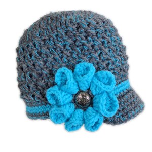 Puede incluir: Sombrero de punto gris y azul con una gran flor azul y un bot&oacute;n plateado.