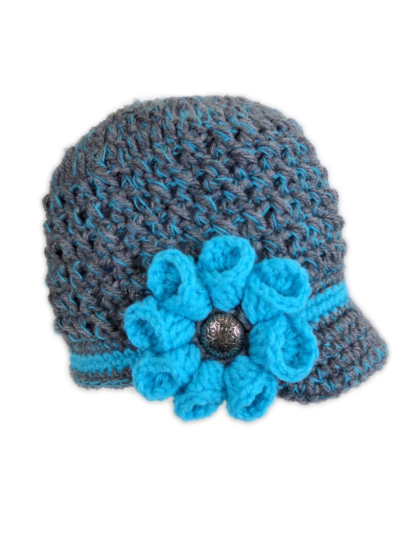 Puede incluir: Sombrero de punto gris y azul con una gran flor azul y un bot&oacute;n plateado.