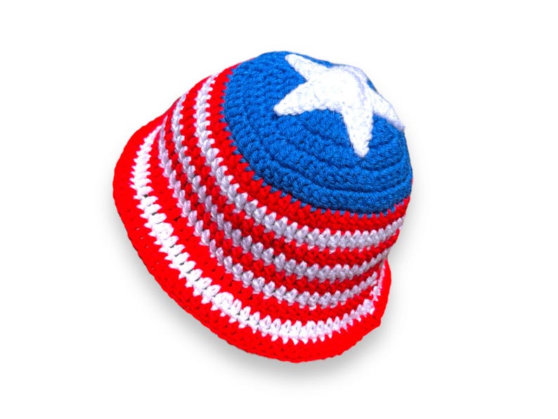 May include: A handmade crochet bucket hat in red, white, and blue. The hat features alternating red and white stripes on the brim and a blue crown with a white star. This patriotic hat is perfect for summer.