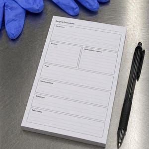 May include: A white notepad with pre-printed sections for surgical procedures, including equipment, position, medications, prep, and dressings. A black pen rests beside the notepad, with blue surgical gloves in the background.