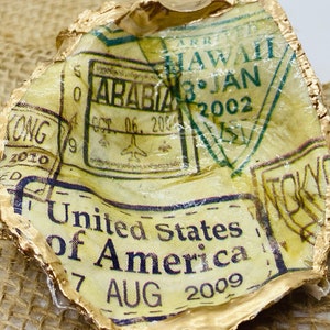 May include: A gold-leafed paperweight with a yellow background and multiple passport stamps. The stamps are from various countries, including Hawaii, Arabia, and the United States of America. The text on the stamps reads "ARR HAWAII 3 JAN 2002", "OCT 06, 200", "United States of America 7 AUG 2009", and "TOKY".