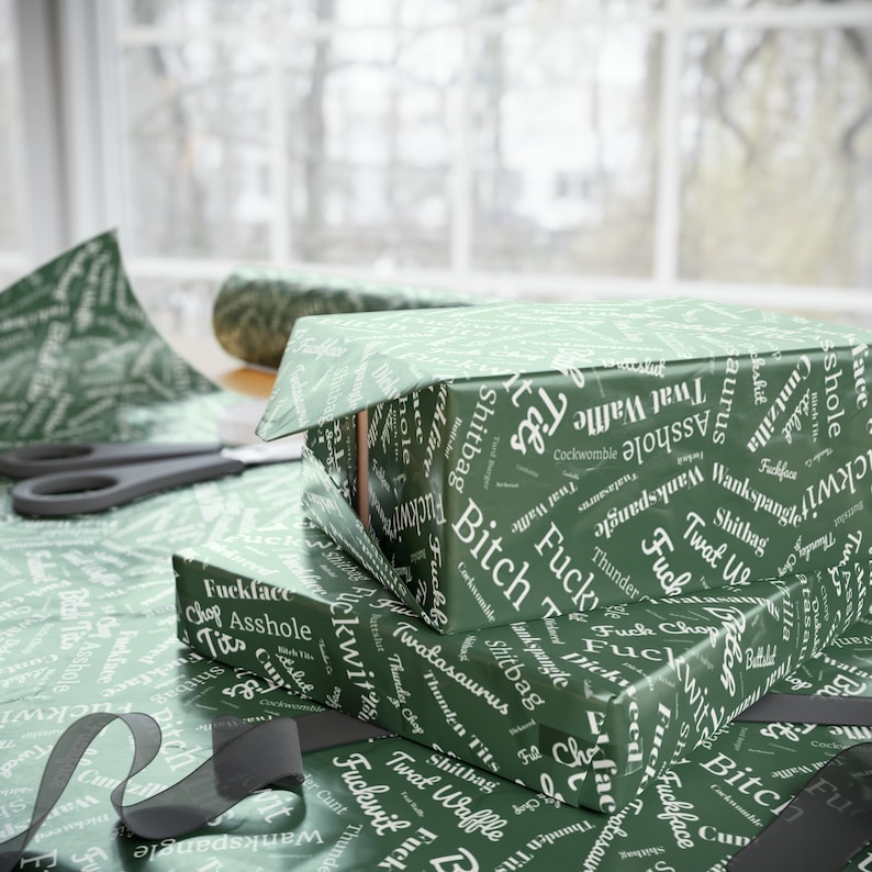 May include: A stack of green gift wrap with a white print of various words, including "bitch", "fuck", "asshole", and "twat".