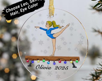 May include: Clear, round Christmas ornament featuring a gymnast in a blue leotard on a balance beam. The beam has colorful lights. The name "Olivia 2025" is printed below. The ornament has a gold ribbon for hanging.