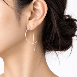 May include: A silver-toned earring featuring a thin, curved semi-circle wire that intersects with a straight, vertical metal bar. The earring is designed to hang from the earlobe, creating a geometric shape with clean lines and a polished finish.