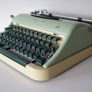 May include: A vintage green and cream typewriter with a green keyboard and a carriage return lever. The typewriter has a label that reads "Olivetti" and "Lettera 30".