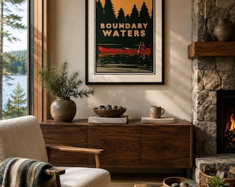 Peut inclure: Une affiche murale encadrée intitulée Boundary Waters représentant une illustration graphique d'un canoë rouge sur une eau sombre avec une silhouette de forêt et un ciel orange. L'affiche est présentée dans un cadre noir.