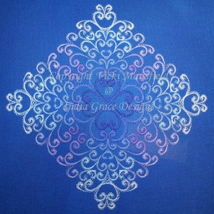 May include: White embroidered design on a blue background. The design features a repeating pattern of swirls and hearts. The text "Copyright Vicki Maske @ India Grace Designs" is visible in the centre of the design.
