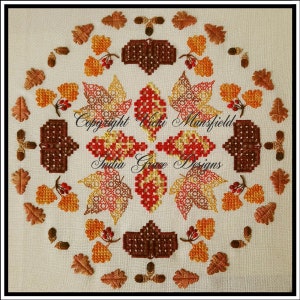 Könnte beinhalten: Ein Kreuzstichmuster mit einem kreisförmigen Design aus Herbstblättern in Rot-, Orange-, Gelb- und Brauntönen. Die Blätter sind von einem Rand aus Eicheln und Eichenblättern umgeben. Der Text "Copyright Vicki Mansfield India Grace Designs" befindet sich in der Mitte des Designs.