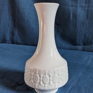 Könnte beinhalten: Weiße Keramikvase mit einem strukturierten, geprägten Design aus Kreisen und Blättern um die Basis.