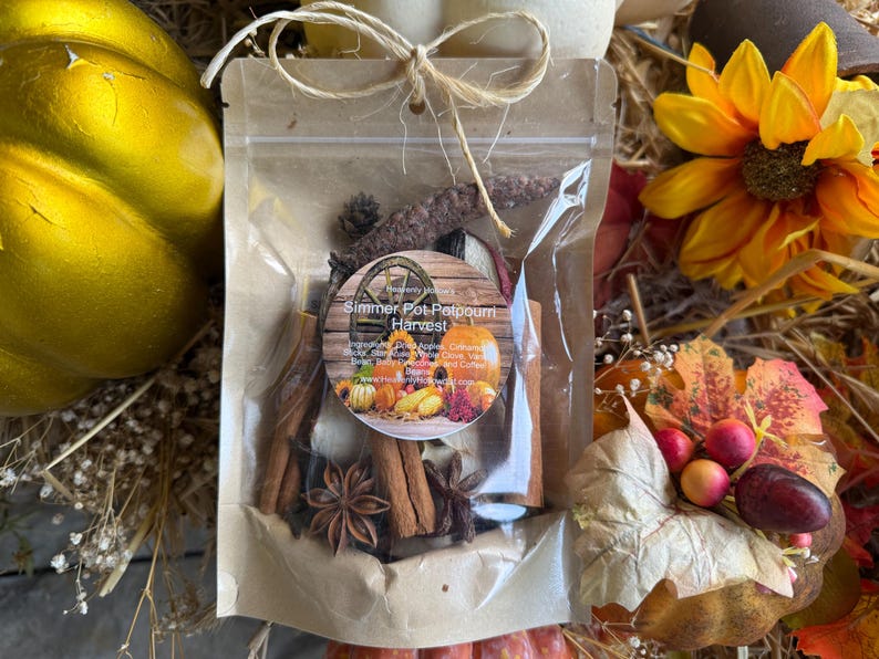 May include: A clear bag tied with twine, filled with potpourri ingredients. The bag features a circular label with the text "Simmer Pot Potpourri Harvest" and images of pumpkins and apples. Cinnamon sticks, star anise, and other dried botanicals are visible.