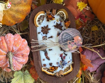May include: A white soy candle in a wooden bowl, decorated with dried fruit, spices, and flowers. The candle is labeled "Pumpkin Spice Soy Candle Bowl". The image includes pumpkins and fall foliage.