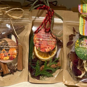 May include: Three bags of potpourri, labelled Harvest, Christmas Memories, and Summer Vibes. The bags are clear and filled with dried botanicals. Each bag is tied with twine or ribbon. The Harvest bag contains cinnamon sticks.