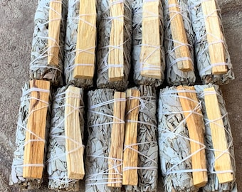 May include: A collection of white sage smudge sticks bundled with palo santo sticks. The sticks are tied together with white string and arranged in rows.