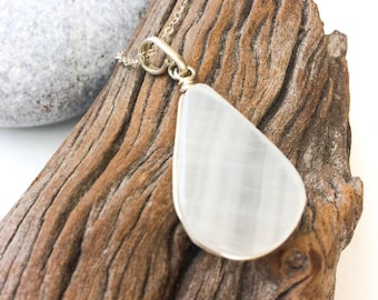 May include: A white teardrop-shaped selenite pendant on a silver chain. The pendant is hanging from a piece of driftwood.