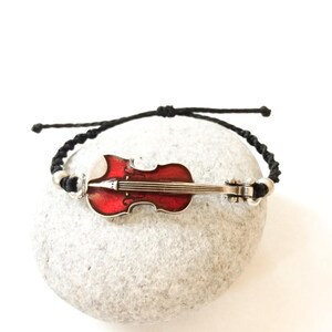 May include: A black string bracelet with a red and silver violin charm.