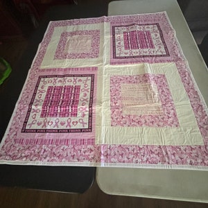 May include: A pink and white quilt with a pink ribbon pattern and the text "Think Pink Think Pink Think Pink" in the center. The quilt is made of squares and rectangles and has a white border.