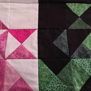 Puede incluir: Primer plano de un edred&oacute;n de patchwork con un dise&ntilde;o geom&eacute;trico. El edred&oacute;n presenta cuadrados de telas blancas, negras y rosas. La tela rosa tiene un patr&oacute;n de remolino. Tambi&eacute;n hay tri&aacute;ngulos verdes con patrones florales y de hojas.