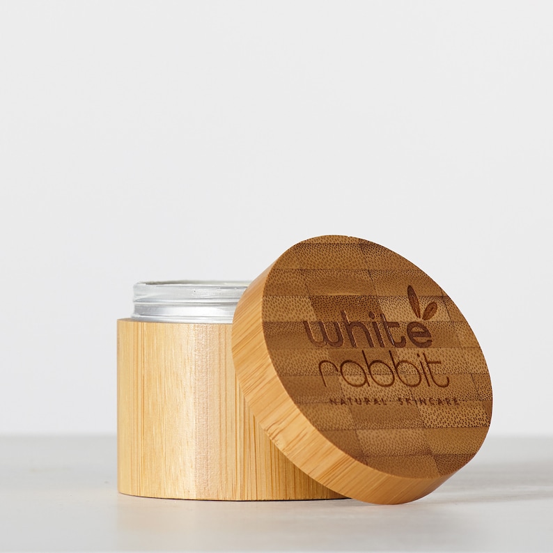 K&ouml;nnte beinhalten: Ein runder Bambusbeh&auml;lter mit einem silbernen Deckel. Der Beh&auml;lter hat ein wei&szlig;es Etikett mit dem Text "white rabbit natural skincare".