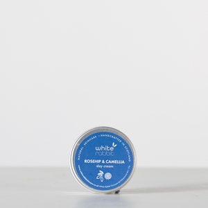 K&ouml;nnte beinhalten: Eine kleine, silberne Dose mit White Rabbit Gesichtscreme f&uuml;r tags&uuml;ber. Die Dose ist mit "Naturkosmetik - Handgefertigt in Schottland" beschriftet und zeigt ein wei&szlig;es Kaninchen-Logo. Das Produkt hei&szlig;t "Rosehip & Camellia Day Cream".