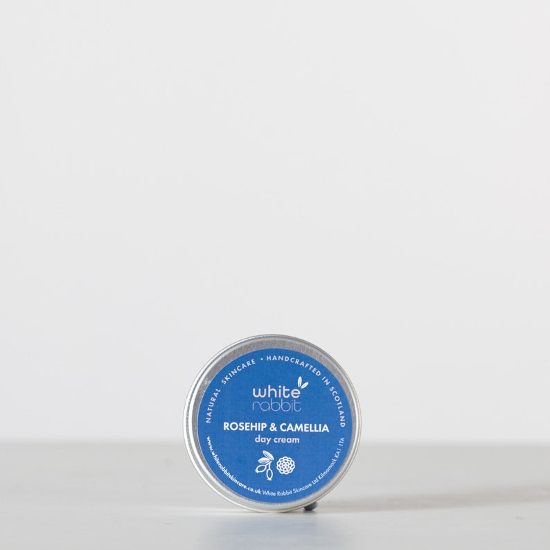 K&ouml;nnte beinhalten: Eine kleine, silberne Dose mit White Rabbit Gesichtscreme f&uuml;r tags&uuml;ber. Die Dose ist mit "Naturkosmetik - Handgefertigt in Schottland" beschriftet und zeigt ein wei&szlig;es Kaninchen-Logo. Das Produkt hei&szlig;t "Rosehip & Camellia Day Cream".