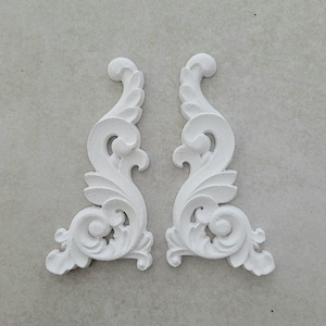 May include: Two white, decorative, ornate, plaster corner mouldings with a floral design.