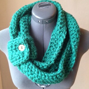 May include: A green crocheted infinity scarf with a small pocket and a button on the front.