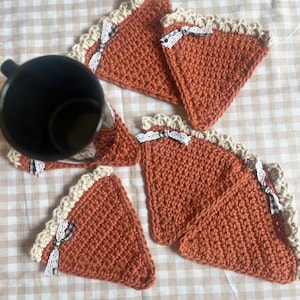 May include: Four crocheted orange and white pie-shaped coasters with white lace trim and black and white ribbon bows.