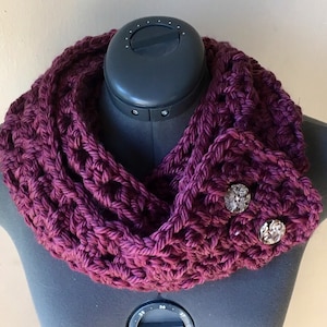 May include: A deep purple crocheted infinity scarf with two decorative buttons.