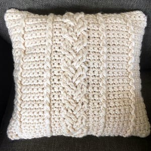 May include: A cream-colored crocheted pillow with a cable knit pattern.