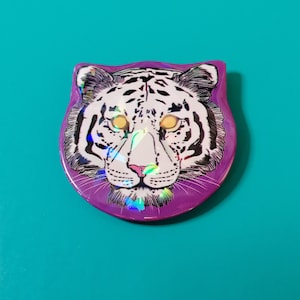 Op de afbeelding: Een paarse knop met een bedrukt wit tijgergezicht. De ogen van de tijger zijn iriserend.