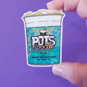 May include: A sticker of a blue and green instant noodle cup with the text "POTS noodle" and "SWEAT & SICK FLAVOUR" with a small bowl of noodles on top. The sticker has a glittery finish and the text "HEART PALPITATIONS - IN 6 MINUTES - 90g" is printed on the bottom.
