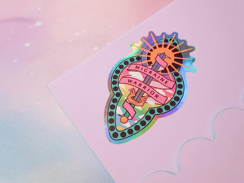 Pu&ograve; includere: Un adesivo olografico con un design rosa e verde. Presenta una spada con ali, un sole e nuvole. Il testo "Migraine Warrior" &egrave; scritto su uno stendardo rosa.